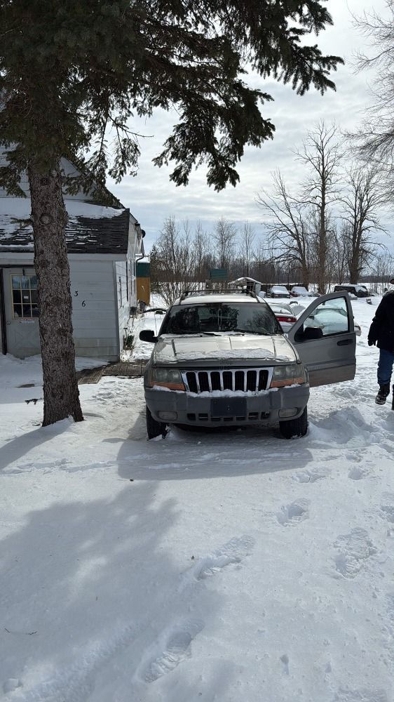 A gold SUV parked in a snowy yard next to a white building, with a person standing by the open driver-side door.