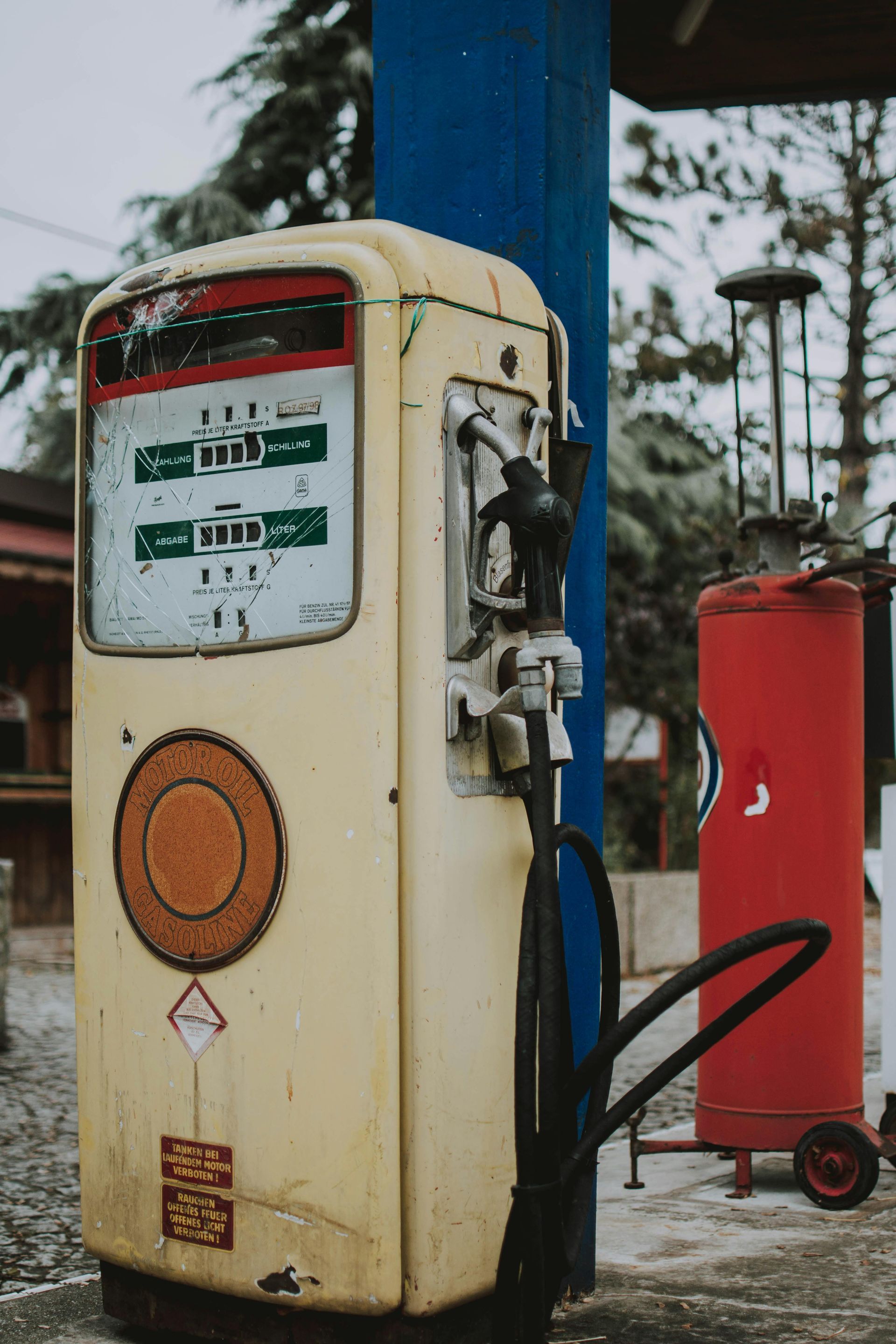 An old gas pump is sitting next to a red tank at a gas station.