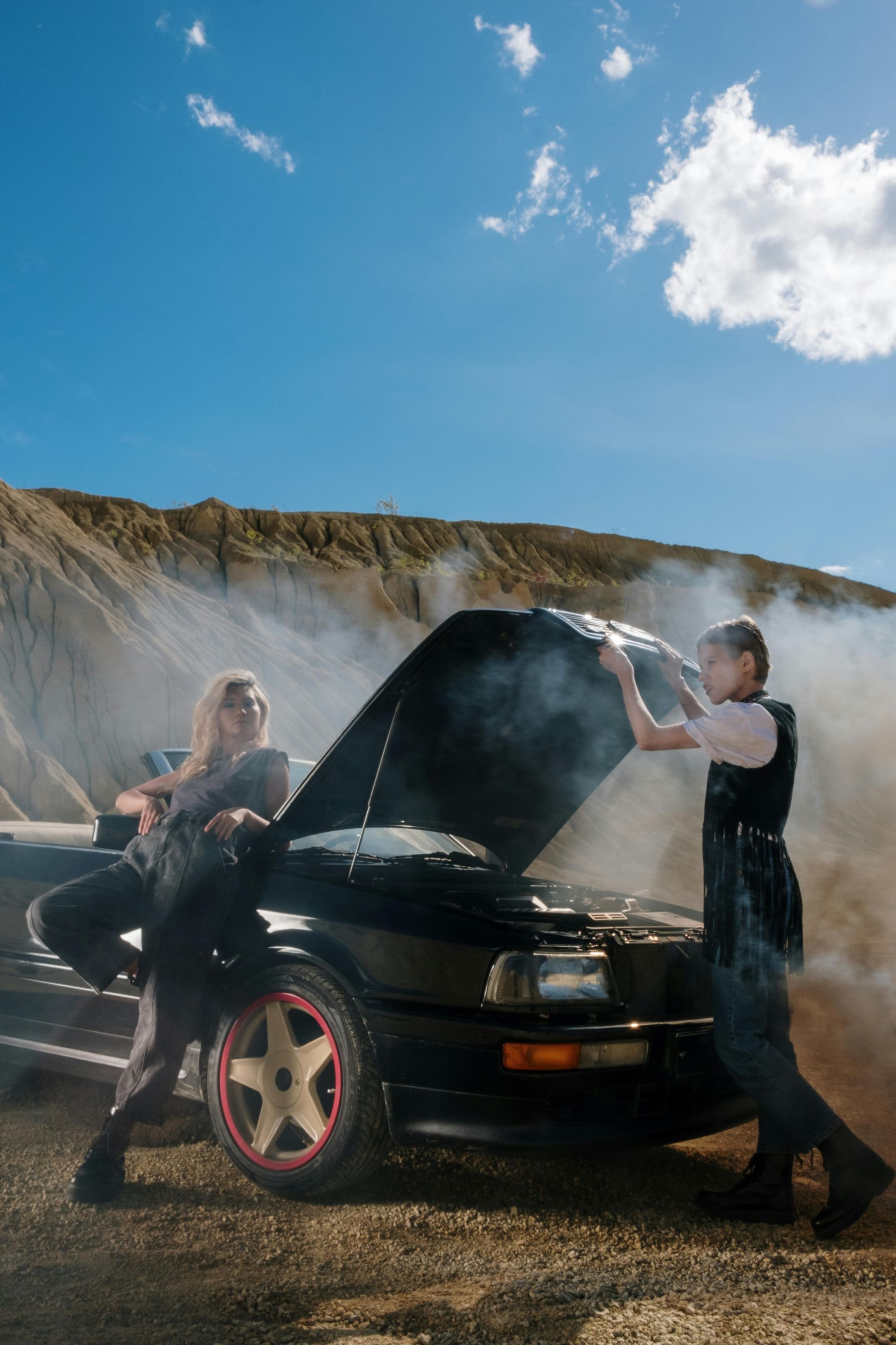 A man and a woman are working on a broken down car.