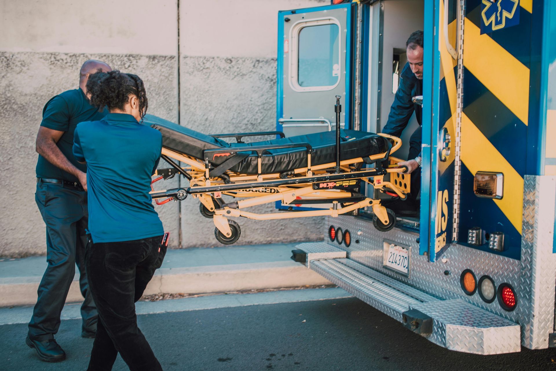 A man and a woman are pushing a stretcher into an ambulance.