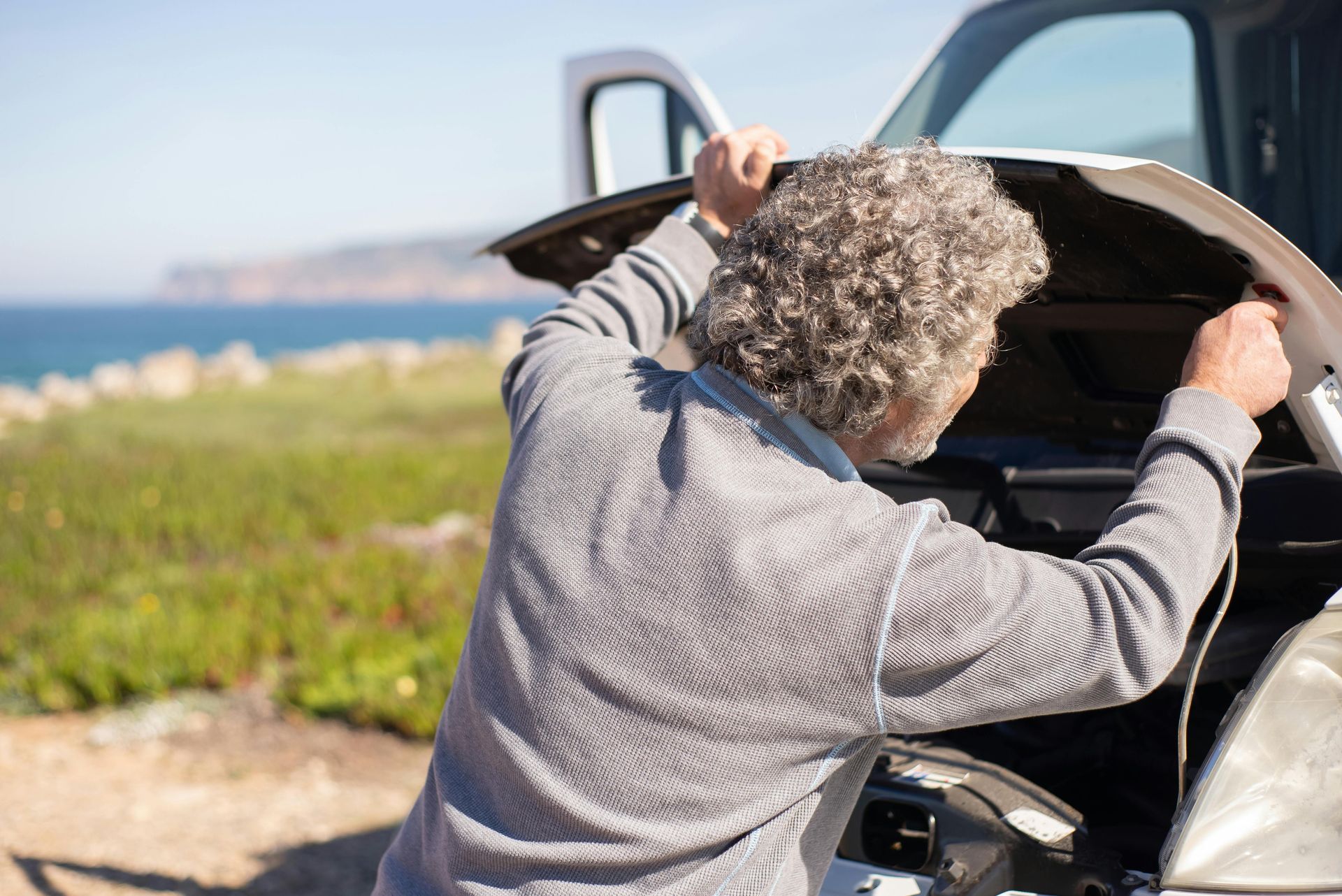 An older man is looking under the hood of his car.