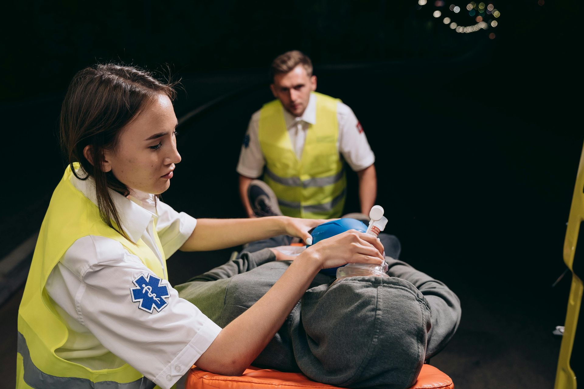 A woman is sitting on a stretcher with a man in the background.