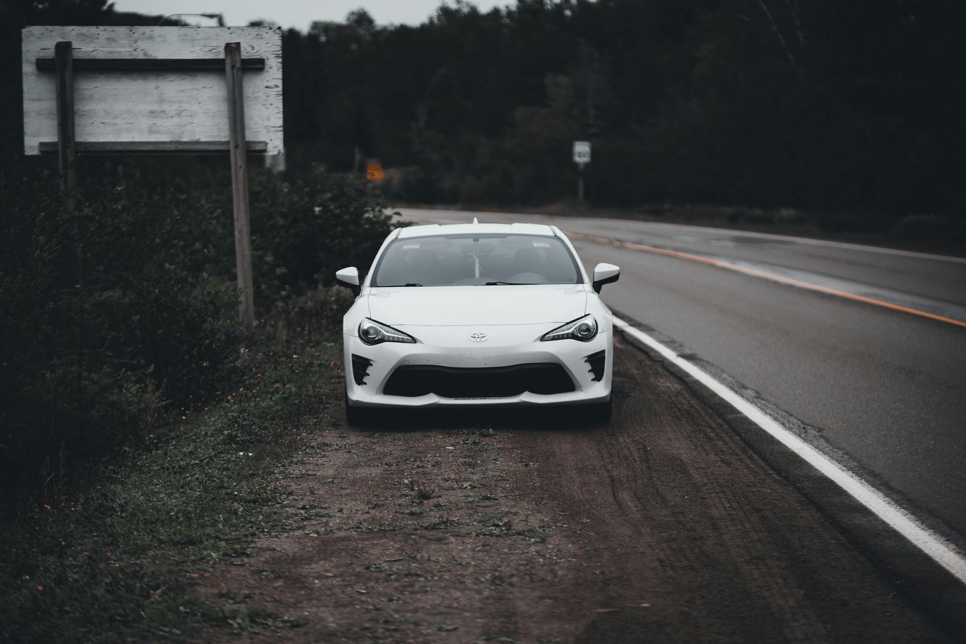A white car is parked on the side of the road next to a sign.