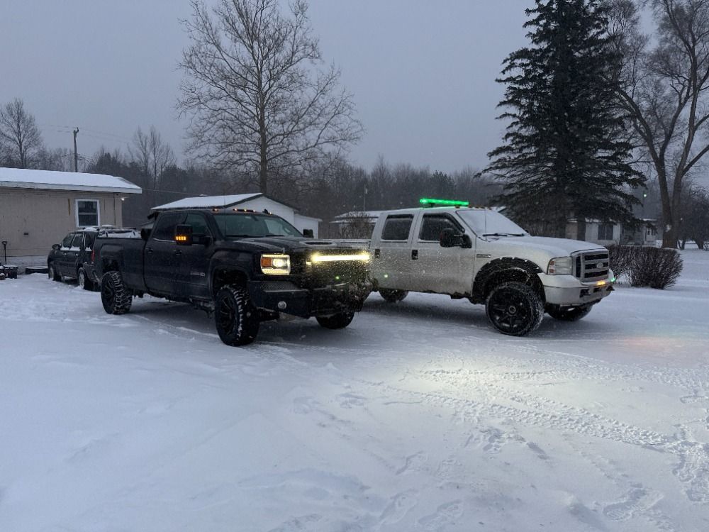 Two trucks are parked in the snow in front of a house.