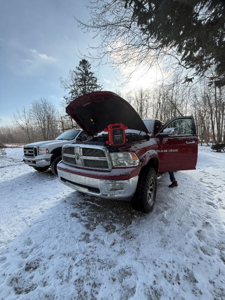 Two trucks are parked in the snow with their hoods open.