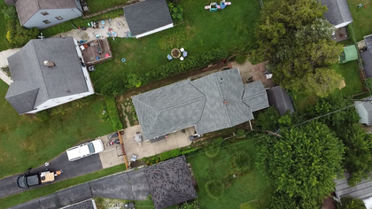 Aerial view of two houses, a driveway, and a green backyard with trees and lawn.
