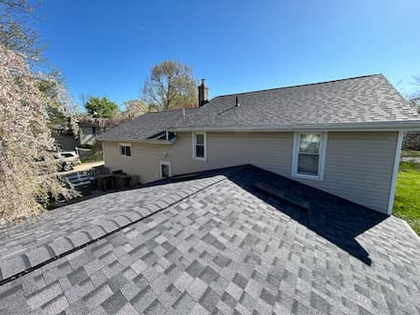 Rooftops and a gray-sided house with trees in the background on a sunny day