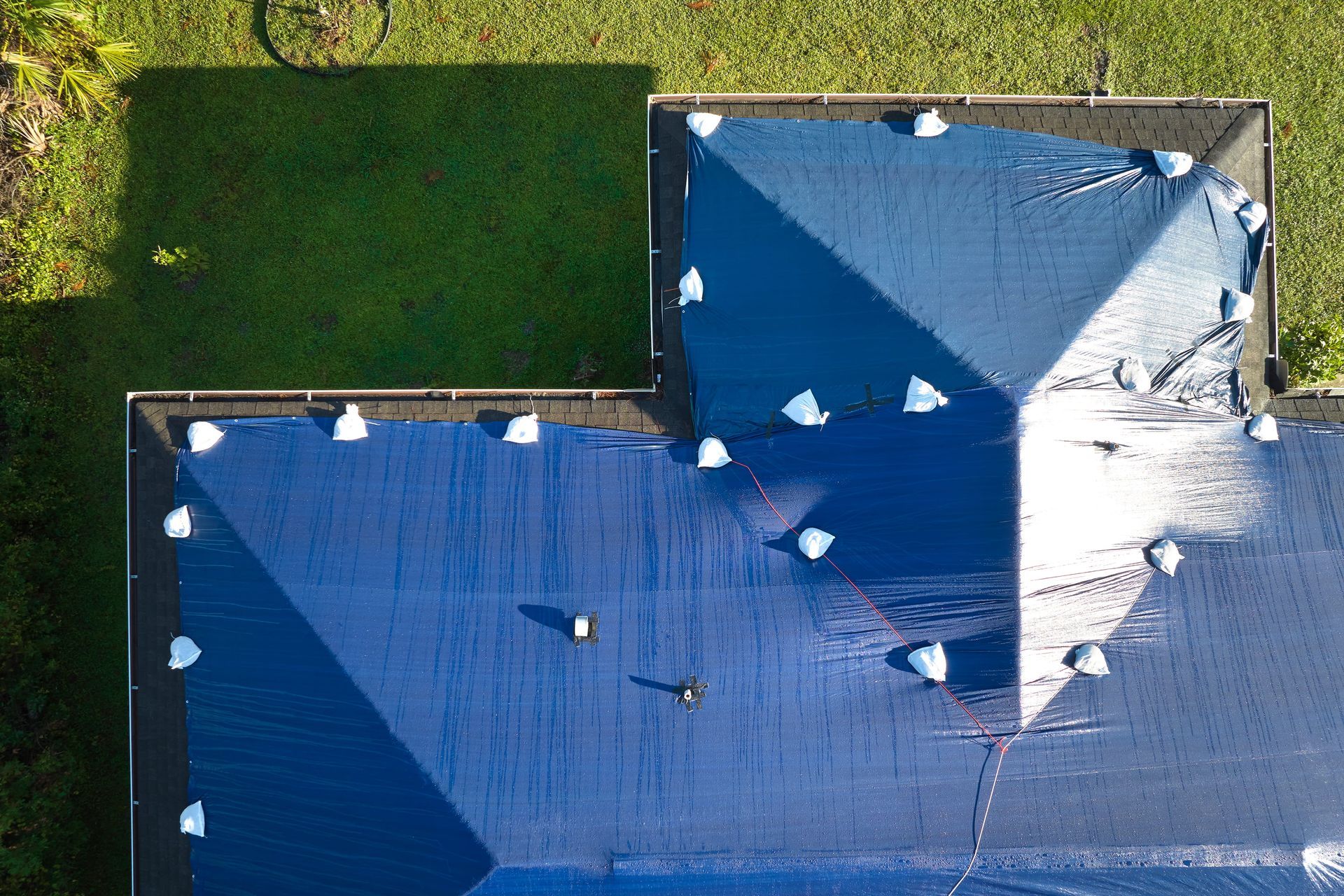 Aerial view of a blue-roofed building beside a green lawn, with bright sunlit shadows.