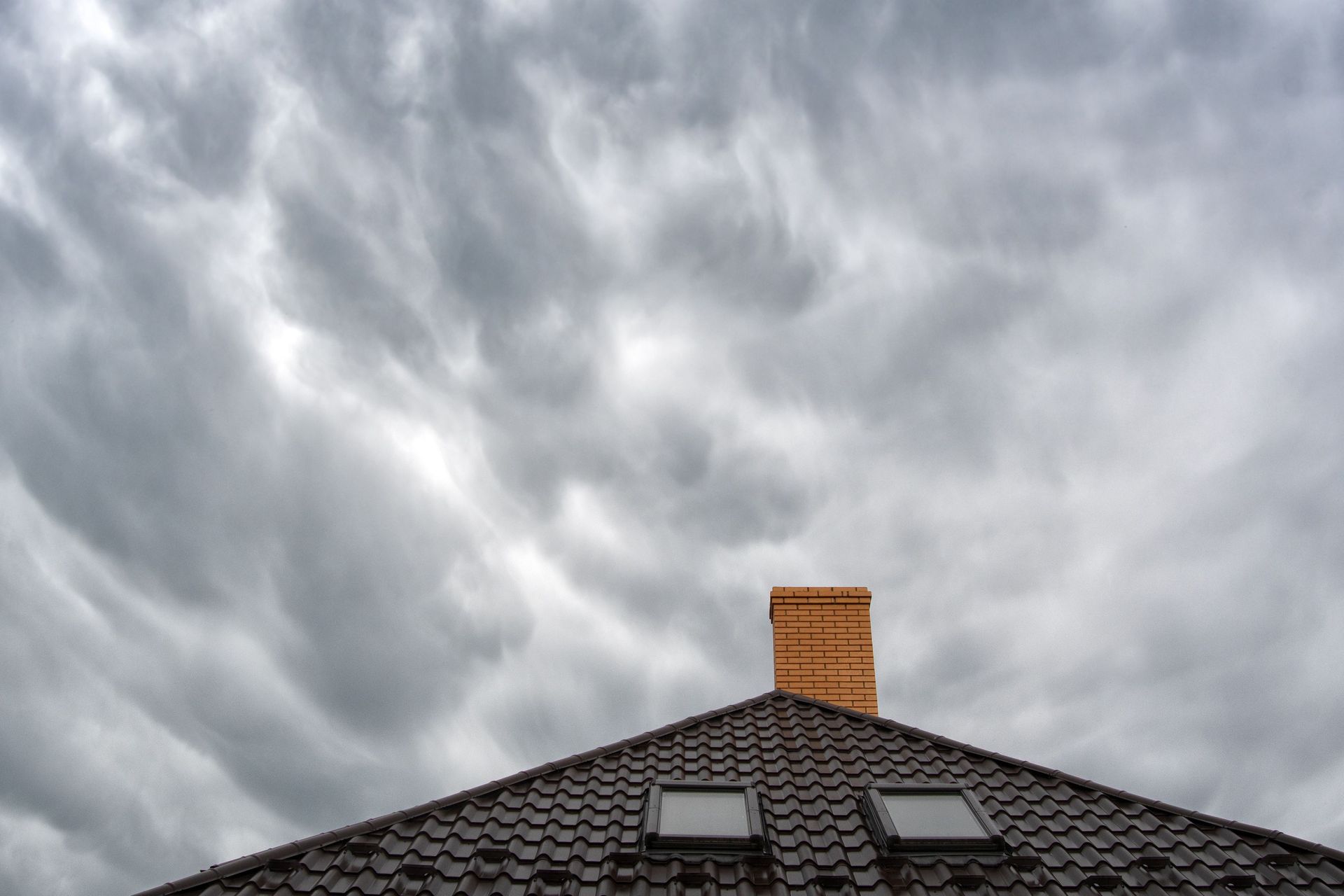 Dark tiled roof with chimney beneath a cloudy gray sky