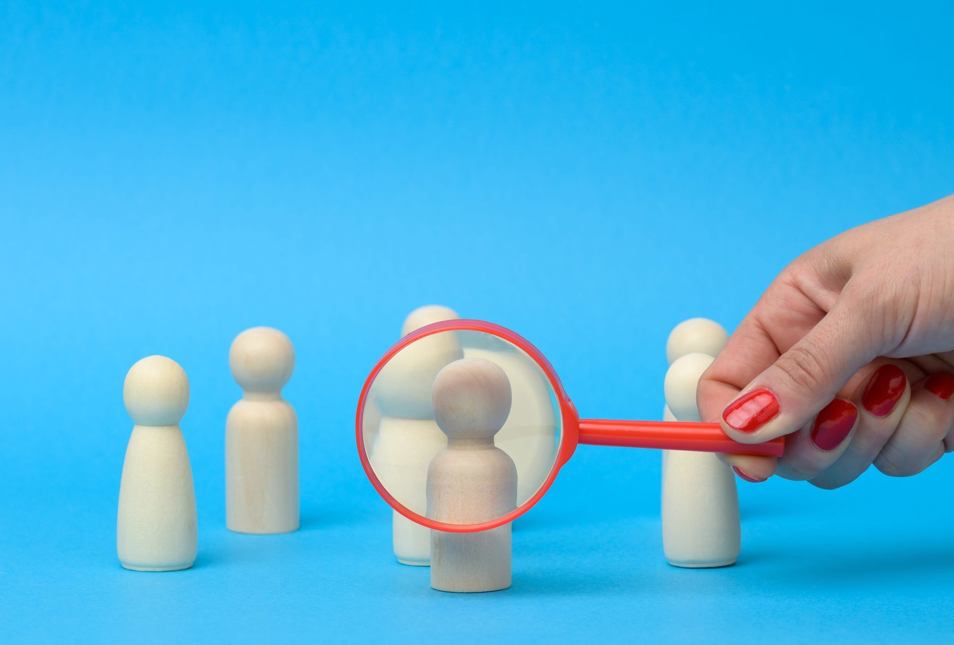 Hand holding magnifying glass over wooden figures on blue background