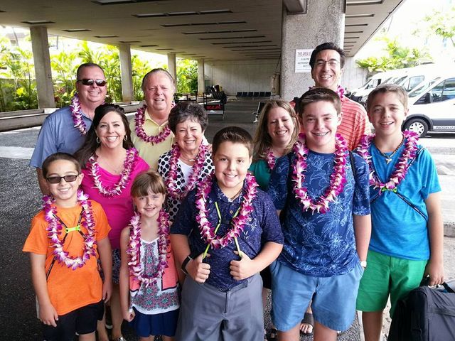 Group of smiling people wearing colorful leis standing under a covered outdoor walkway