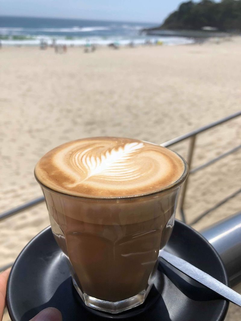 A Cup Of Coffee On A Saucer In Front Of A Beach — Beach Bums Cafe In Forster, NSW