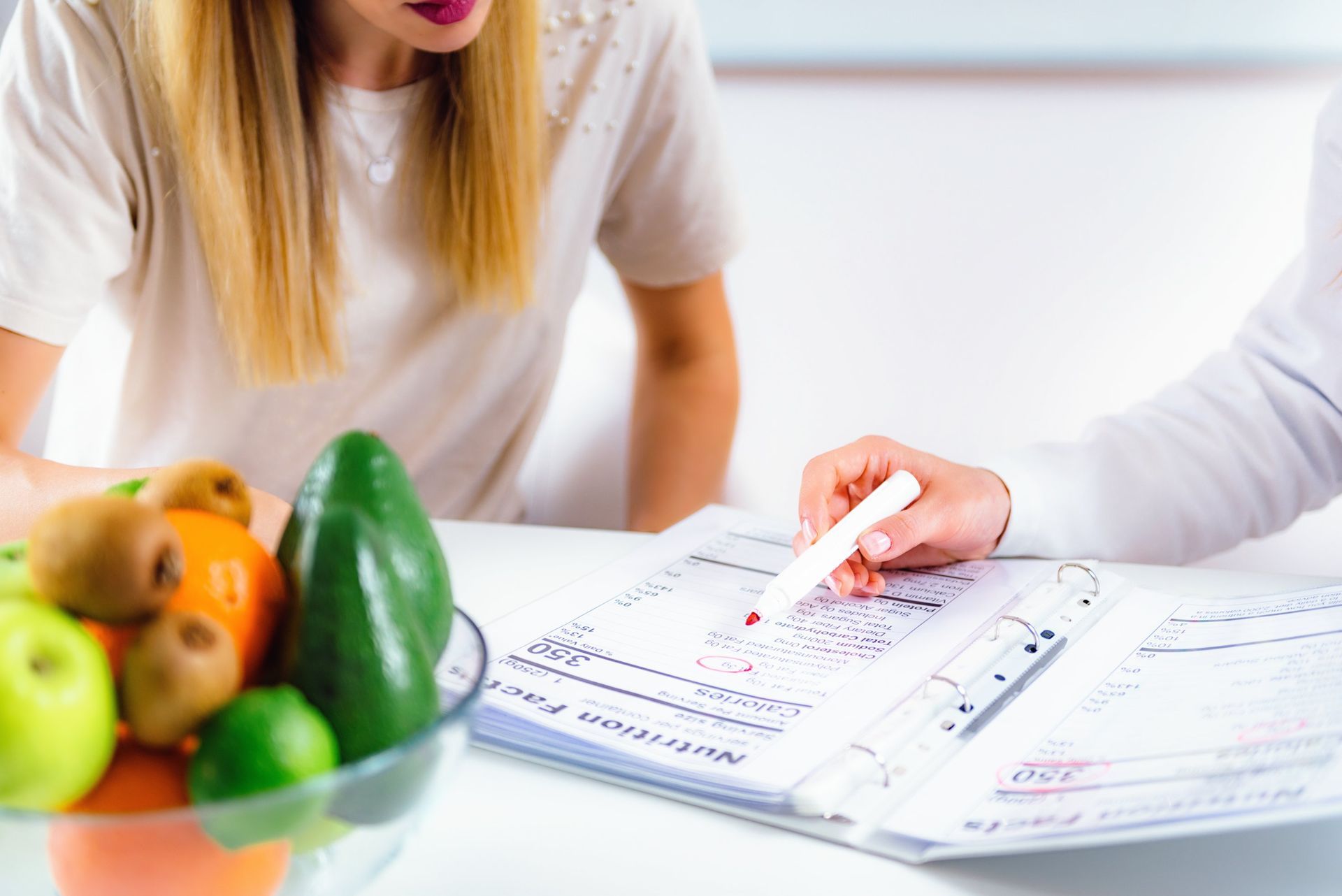 Woman consults with a health professional, looking at a food plan next to a bowl of fruit.