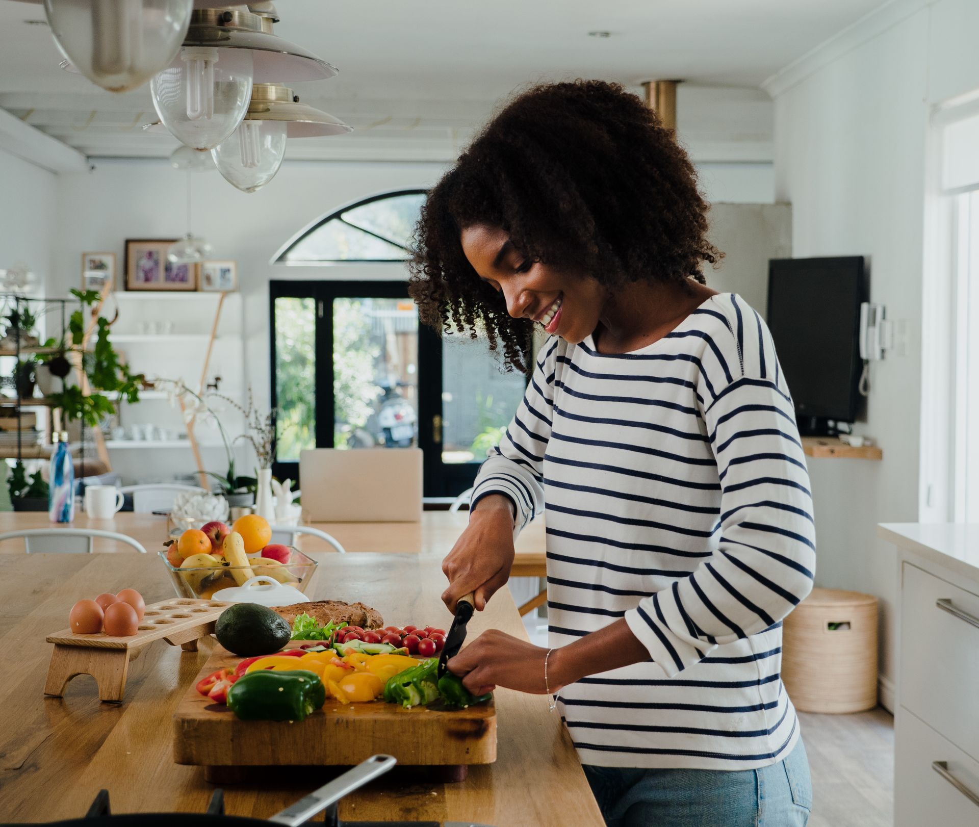 Couple cooking together in a kitchen. Woman grinds pepper over food. Man smiles nearby.