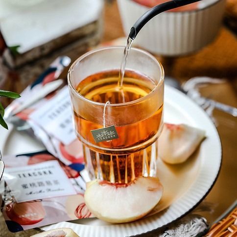 A glass of tea with a tea bag, peaches, and water being poured.