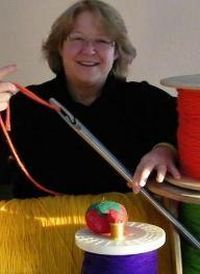 Pam, the inventor, smiling while using a tool near spools of brightly colored yarn