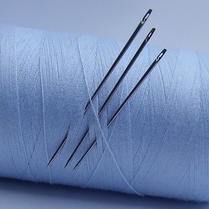Three sewing needles stuck in a spool of light blue thread