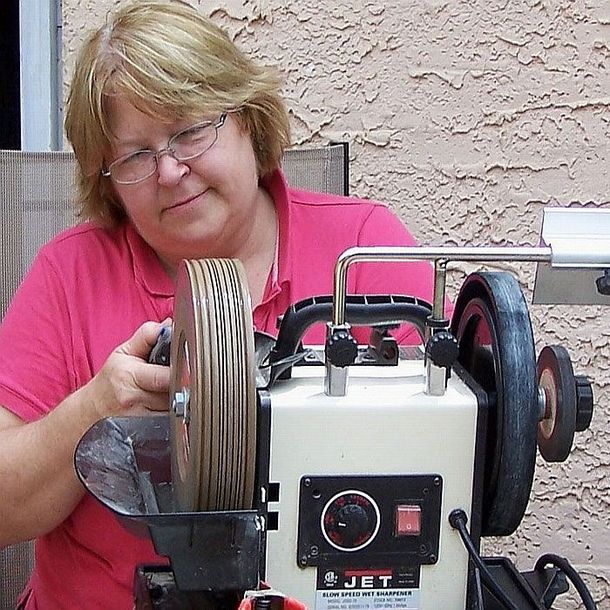 Pam in a pink shirt operating a Dremel machine with large spools of wire or cable outdoors