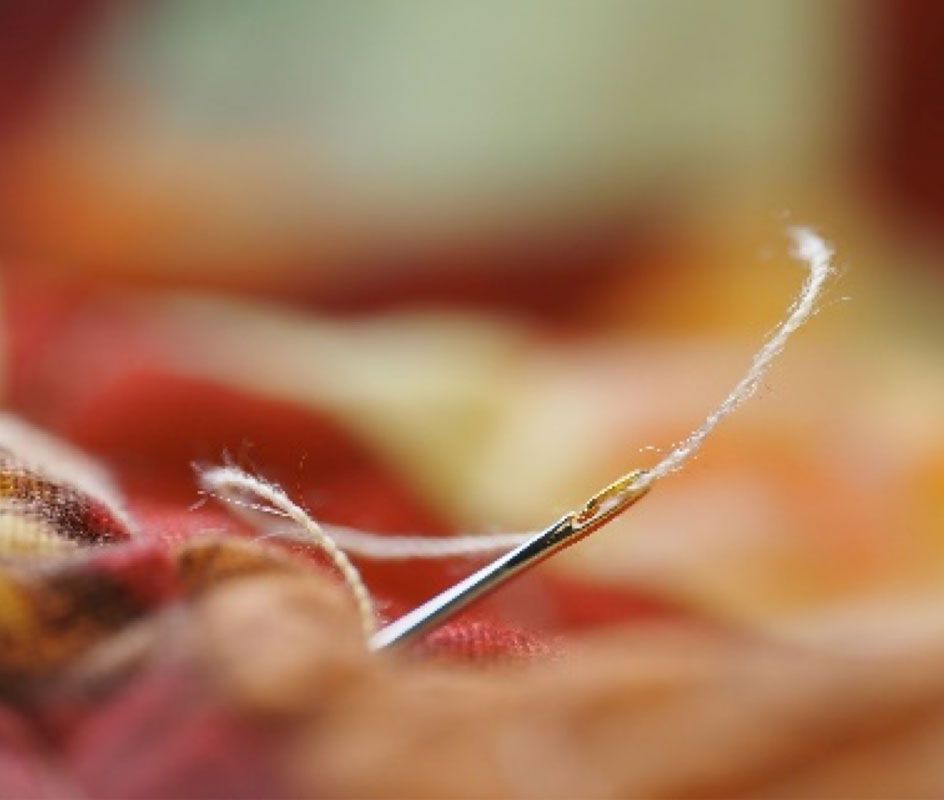 Close-up of a sewing needle threading white fiber through red fabric