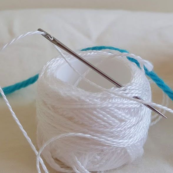 Purple ribbon threaded through a sewing needle on a fabric surface
