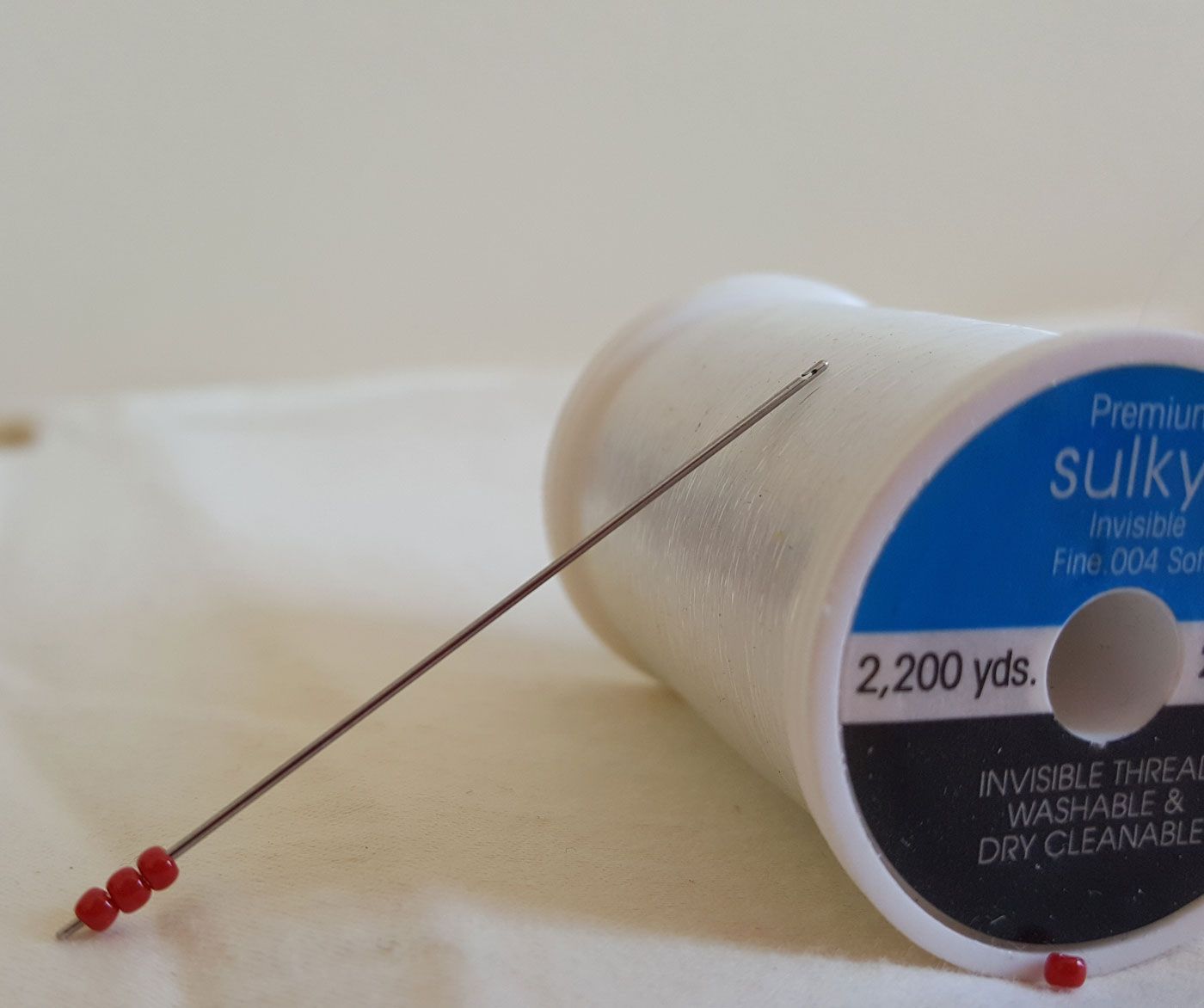 Thread spool with a sewing needle and red beads on the tip, lying on a light surface.