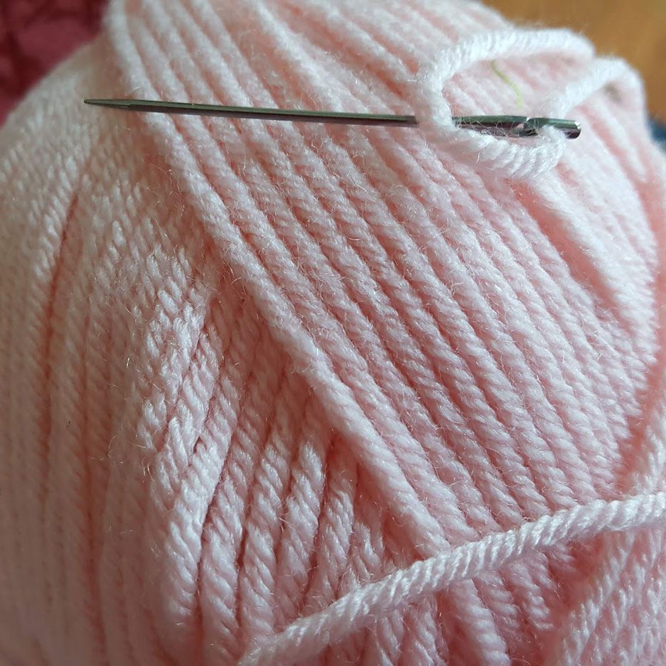 Sewing needle resting on a ball of pale pink yarn