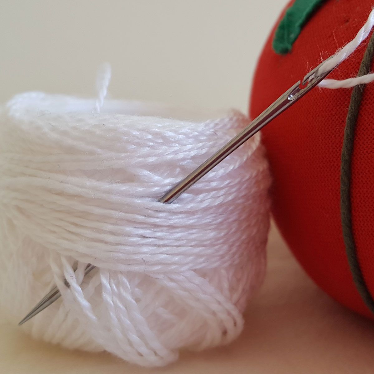 White thread wound around sewing needles beside a red pincushion