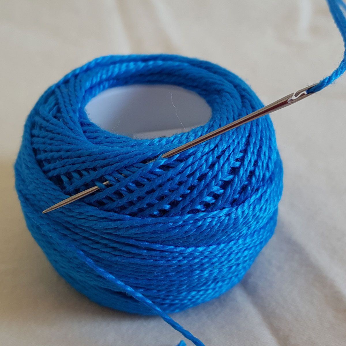 Blue thread wrapped around a spool with a needle inserted through it