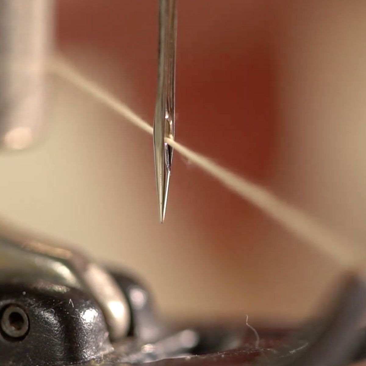 Close-up of a sewing machine needle piercing fabric against a warm background