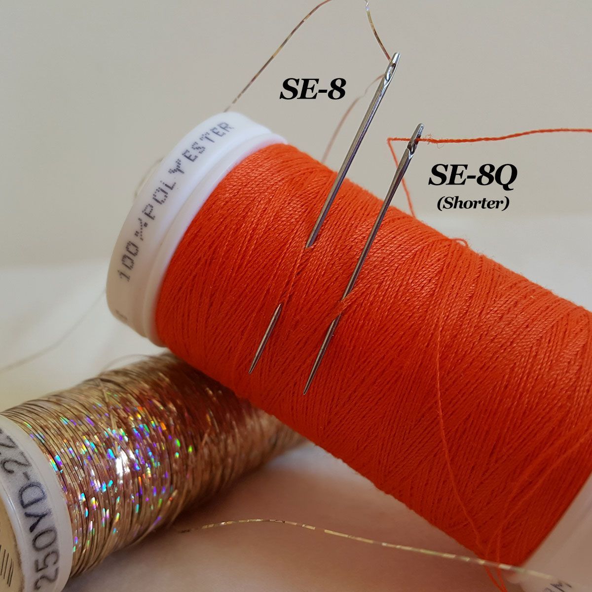 Orange SE-8 and SE-8Q thread spools beside a gold iridescent spool on a white surface