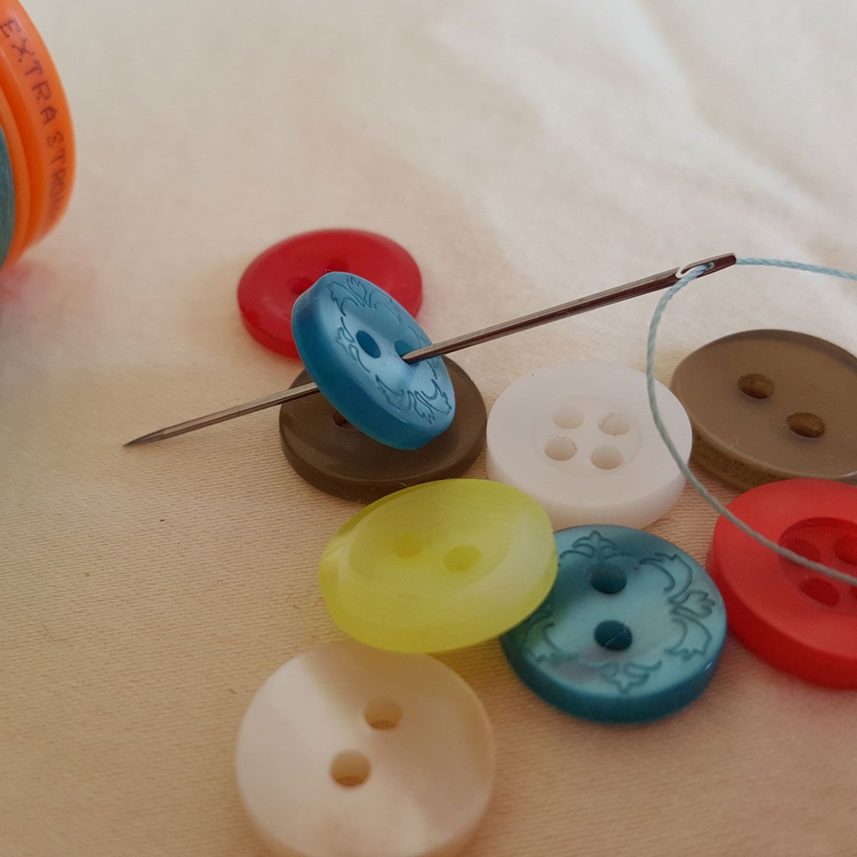 Orange and blue thread spools with a needle on a light surface