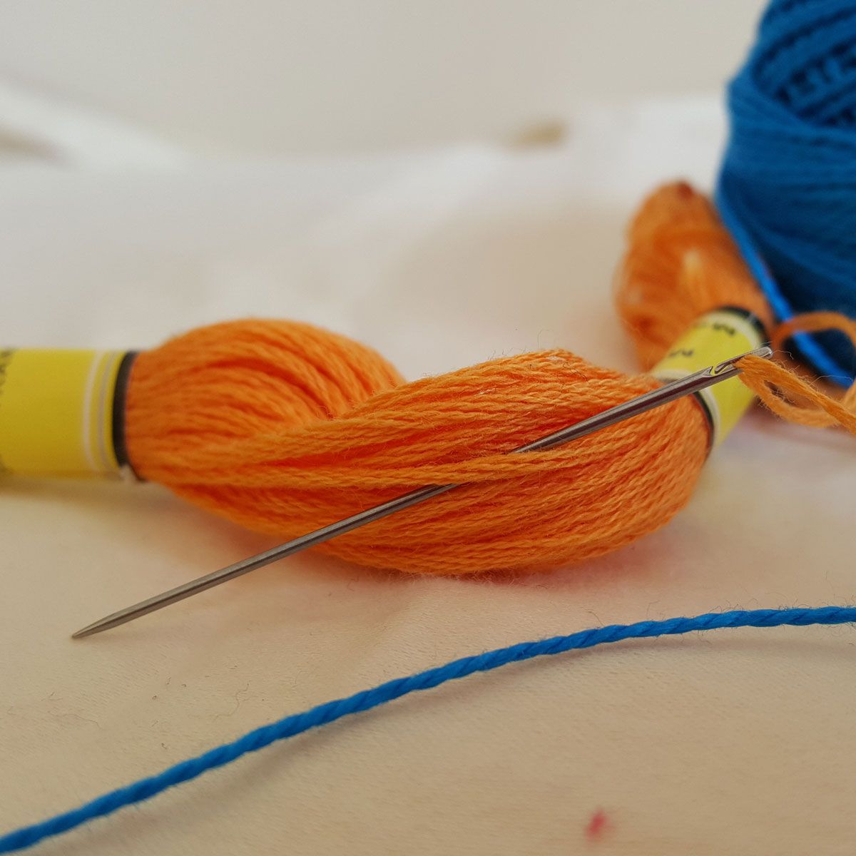 Orange and blue thread spools with a needle on a light surface