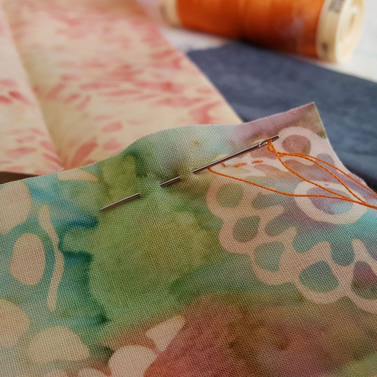 Close-up of a needle and orange thread on patterned fabric during sewing