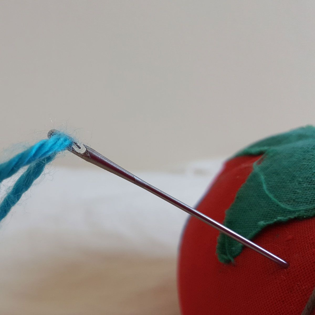 Colorful needlework canvas with a needle and thread laid across blue, green, yellow, and orange stitches