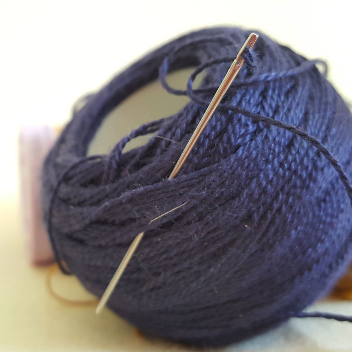 Dark blue ball of yarn with a knitting needle threaded through it.