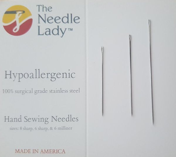 Several metal sewing needles on beige fabric, with a partial 