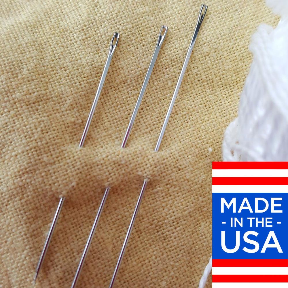 Several metal sewing needles on beige fabric, with a partial 