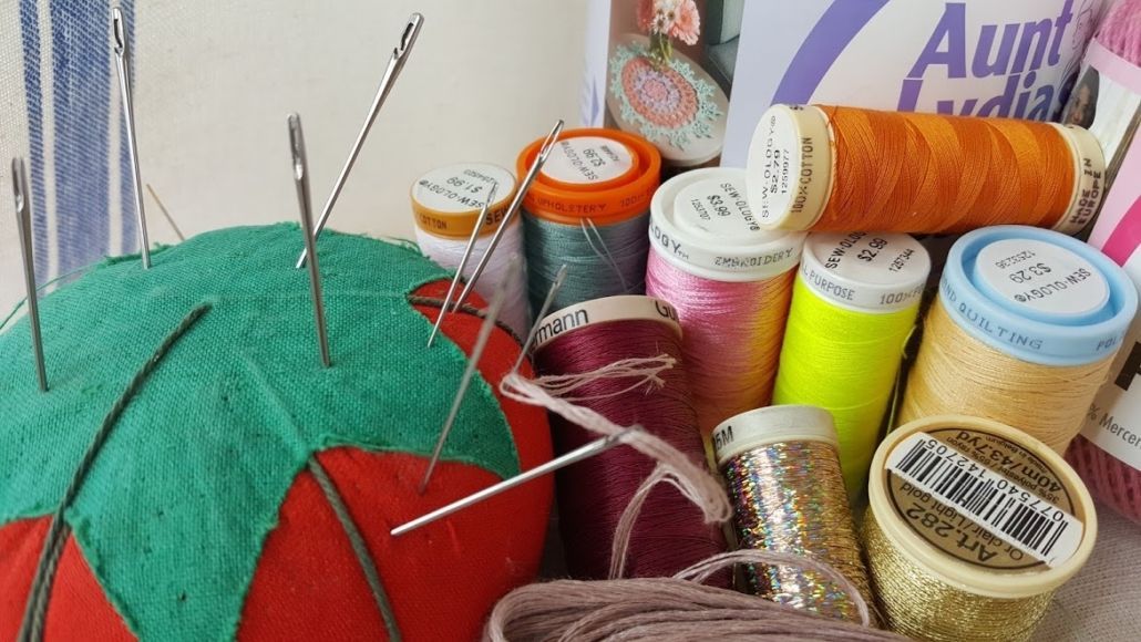 Spool of green foam with many sewing pins and colorful thread spools nearby