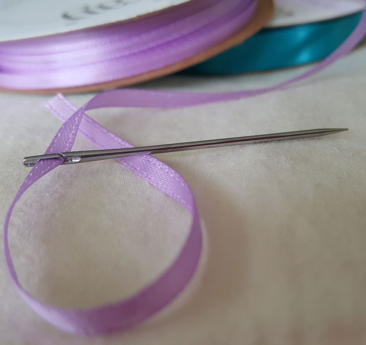 Purple ribbon threaded through a sewing needle on a fabric surface