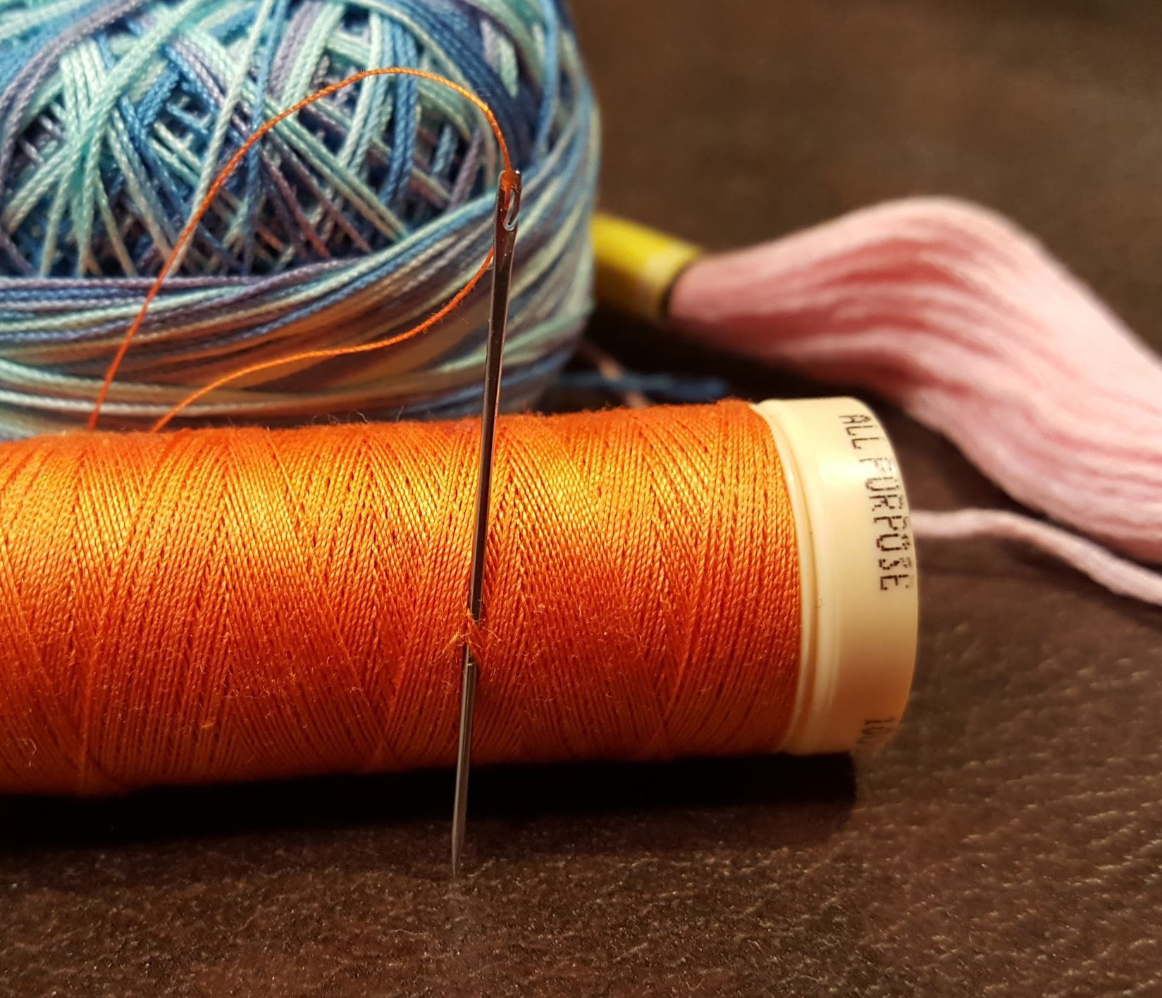 Two spools of thread, gold and burgundy, with a needle and loose thread on a white surface