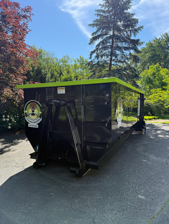 A dumpster is parked in front of a brick building.