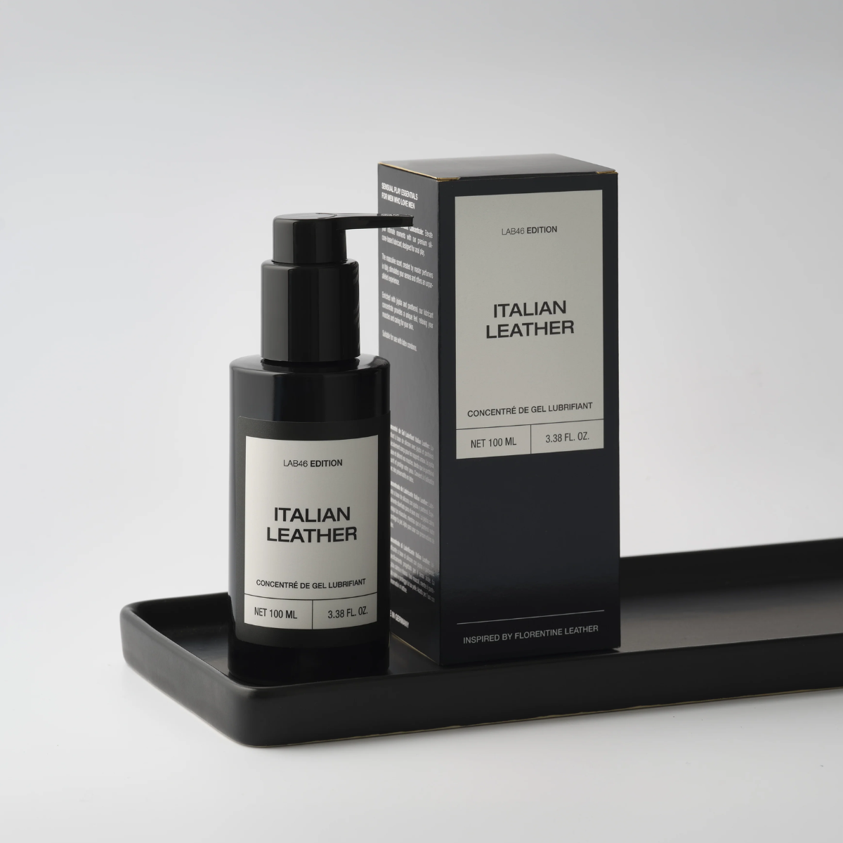Flakon und Schachtel des Parfums „Black Italian Leather“ auf einem Tablett vor grauem Hintergrund