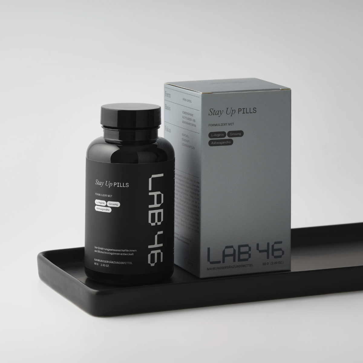 Schwarze Nahrungsergänzungsflasche neben einer grauen LAB 46-Box auf einem schwarzen Tablett vor hellem Hintergrund