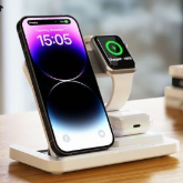 Estación de carga blanca con un iPhone, un Apple Watch y auriculares cargándose.
