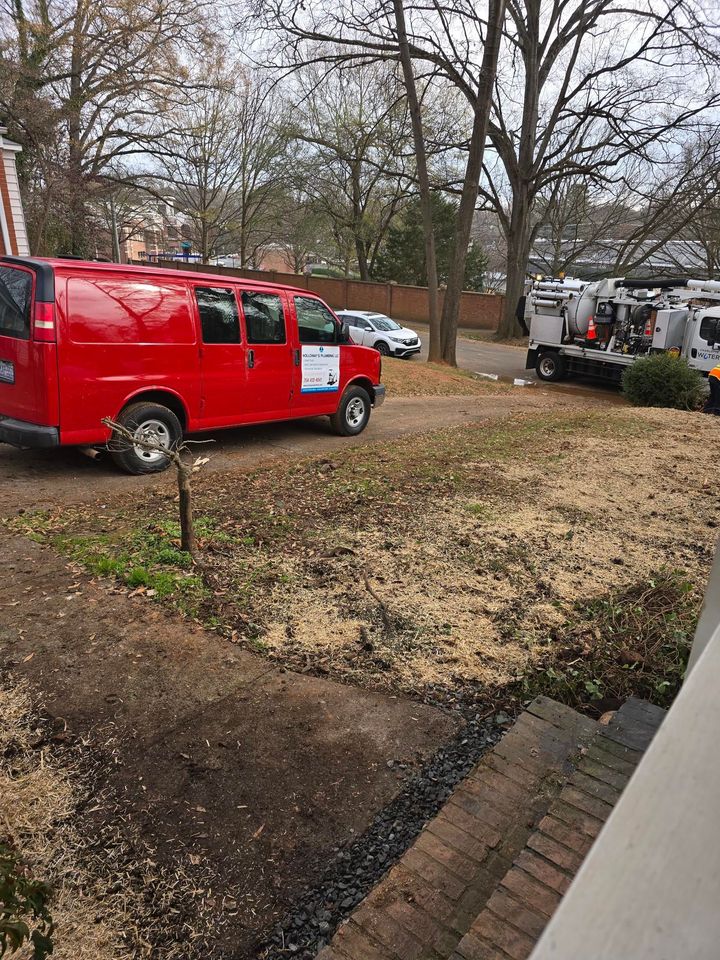 Red utility van parked by a driveway near trees, with emergency trucks in the background.