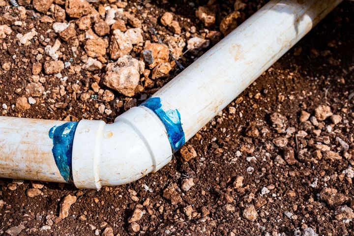 White PVC pipe joint leaking blue sealant in brown soil, close-up of underground plumbing repair
