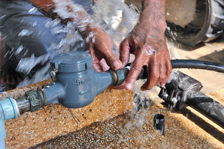 Hands tightening a hose fitting with water spraying over a blue pipe connection