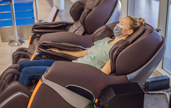 Woman wearing a mask relaxing in a brown massage chair at an airport.