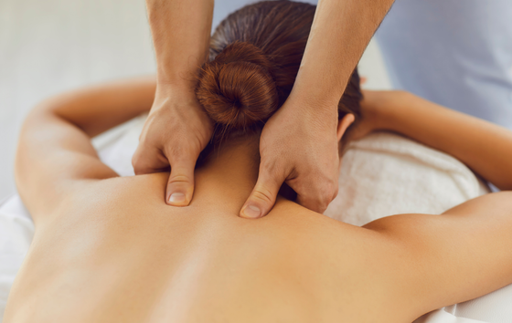 Back of a person receiving a shoulder massage from a masseuse; spa setting, hands working.
