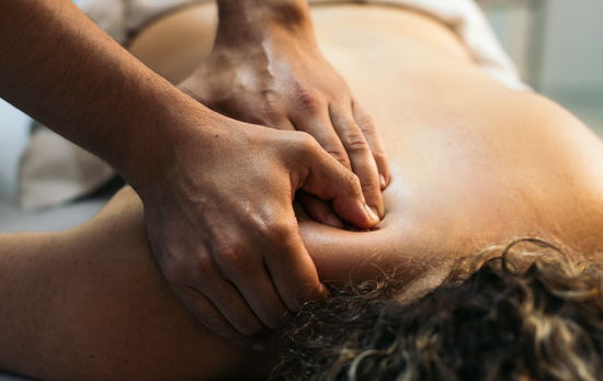 Hands massaging a person's upper back and shoulder in a spa-like setting.